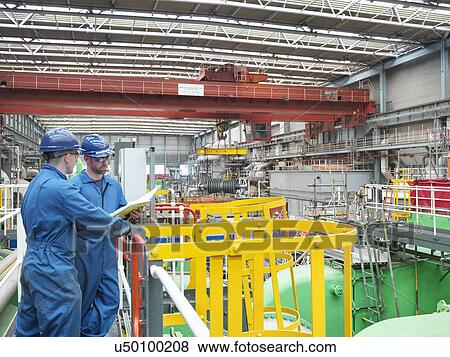 Stock Photo - Engineers discussing notes on walkway during power station outage. Fotosearch