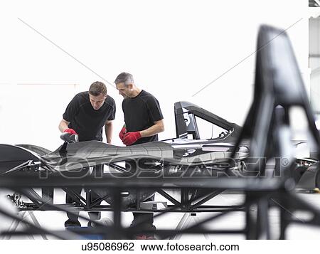 Stock Image - Engineers inspecting carbon fibre car body shell in sports car factory. Fotosearch