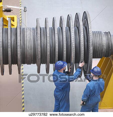 Stock Image - Engineers inspecting turbine during power station outage, high angle view. Fotosearch