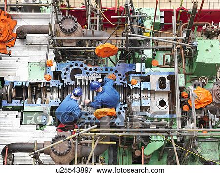 Stock Photo -  Engineers inspecting turbine housing repair during power station outage, overhead view. Fotosearch