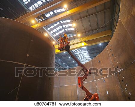 Stock Image - Engineers on high lift inspecting marine fabrication used for cable laying. Fotosearch