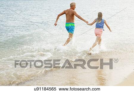 Stock Photography - Father and daughter running and holding hands on beach. Fotosearch