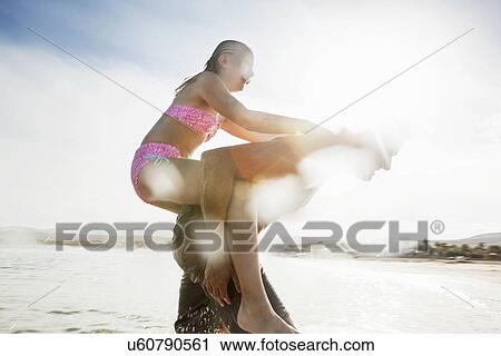 Stock Image - Father giving daughter piggy back on beach. Fotosearch