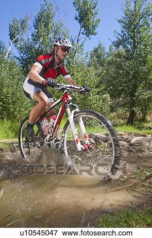 Stock Photo - Female cyclist riding across stream. Fotosearch