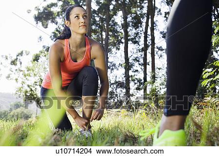 Picture - Female jogger tying shoelace in forest. Fotosearch