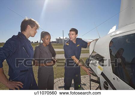 Stock Image - Flight instructor showing student pilots engine of helicopter. Fotosearch