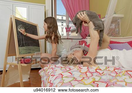 Girl drawing on blackboard whilst mother on bed with cat View Large Photo Image Stock Image - Girl drawing on blackboard whilst mother on bed with cat. Fotosearch