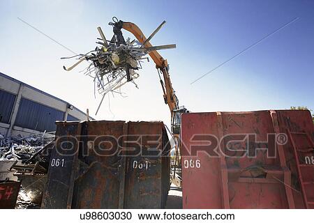 Stock Image - Grapple handler sorting and moving metals into scrap yard container. Fotosearch