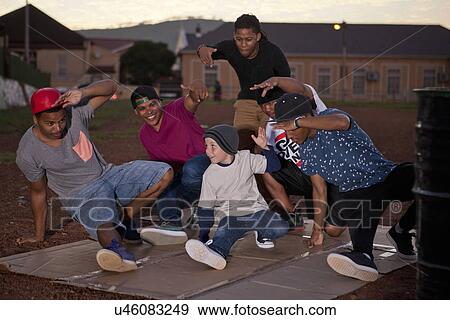 Stock Photo - Group of adult males and boy breakdancing in park at dusk. Fotosearch