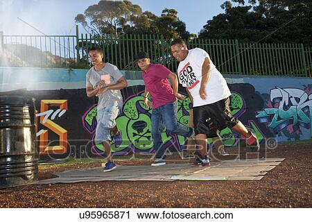 Stock Image - Group of four men breakdancing in park at dusk. Fotosearch