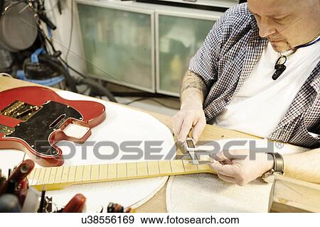 Stock Photo - Guitar maker checking guitar neck in workshop. Fotosearch