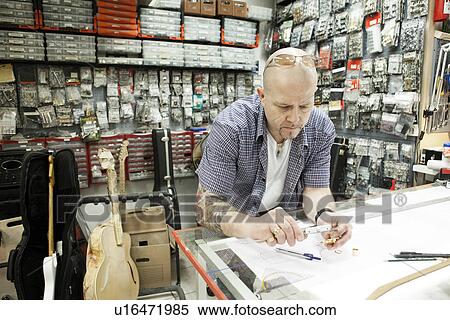 Stock Photography - Guitar maker measuring up blueprint design in workshop. Fotosearch
