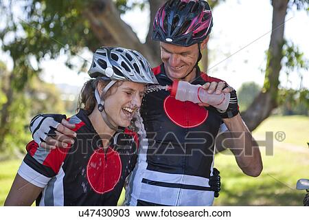 Stock Image - Male cyclist squirting water at woman's face. Fotosearch