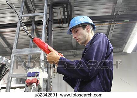 Stock Image - Male electrician checking power supply cable in factory. Fotosearch