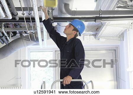 Stock Image - Male engineer checking industrial pipework in factory. Fotosearch