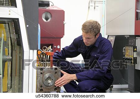 Stock Photo - Male engineer maintaining manufacturing machine in factory. Fotosearch