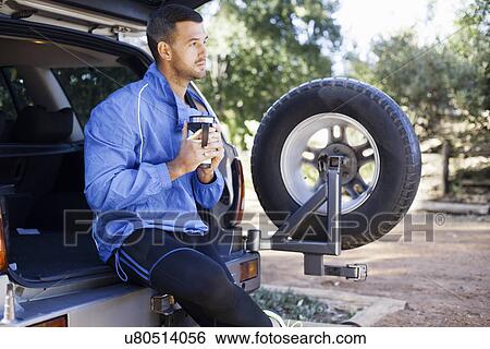 Stock Photograph - Male jogger holding flask at back of car. Fotosearch