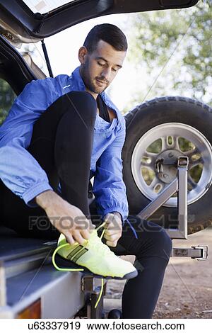 Stock Photo - Male jogger tying shoelace at back of car. Fotosearch