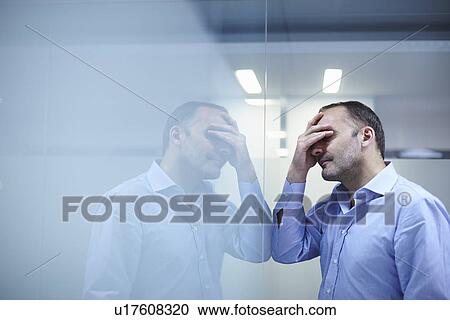 Stock Image - Man in despair facing reflective wall. Fotosearch
