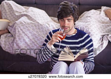 Stock Image - Man reading as two women sleep in yacht cabin. Fotosearch