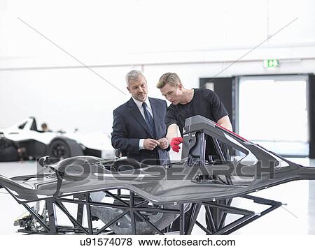 Stock Photo - Manager and engineer inspecting carbon fibre body of supercar in sports car factory. Fotosearch