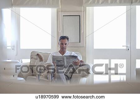 Stock Photo - Mature man reading newspaper in sitting room. Fotosearch