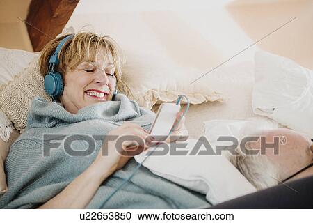 Mature woman lying on bed using mp3 player View Large Photo Image Stock Image - Mature woman lying on bed using mp3 player. Fotosearch
