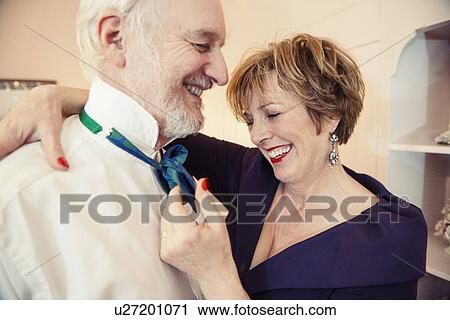 Stock Image - Mature woman putting bow tie on senior man. Fotosearch