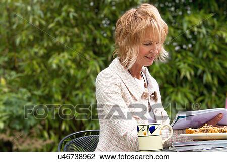 Stock Image - Mature woman reading magazines and having a break in garden. Fotosearch