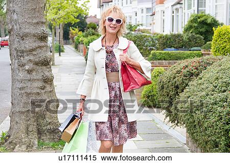 Stock Photography - Mature woman strolling down street with shopping bags. Fotosearch