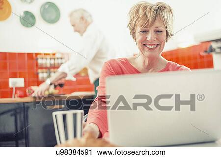 Mature woman using laptop in kitchen View Large Photo Image Stock Image - Mature woman using laptop in kitchen. Fotosearch