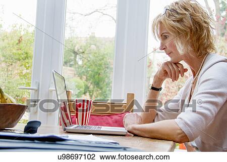 Mature woman using laptop in kitchen View Large Photo Image Stock Image - Mature woman using laptop in kitchen. Fotosearch