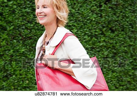 Mature woman walking briskly with red shoulder bag View Large Photo Image Stock Image - Mature woman walking briskly with red shoulder bag. Fotosearch