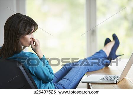 Stock Photography - Mature woman with feet up on desk. Fotosearch