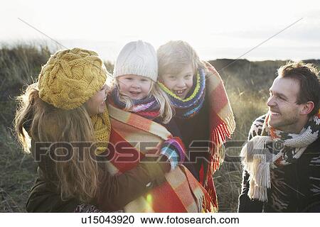 Stock Image - Mid adult couple in sand dunes with their son and daughter wrapped in blanket. Fotosearch