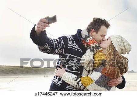 Stock Photo - Mid adult couple taking self portrait with smartphone on beach, Bloemendaal aan Zee, Netherlands. Fotosearch