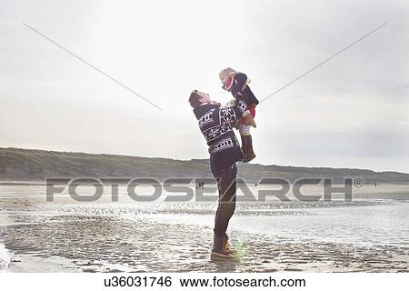 Stock Photograph - Mid adult man lifting up daughter on beach, Bloemendaal aan Zee, Netherlands. Fotosearch