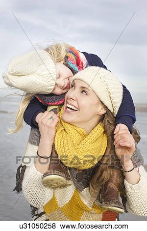 Stock Photo - Mid adult woman carrying daughter on shoulders at beach, Bloemendaal aan Zee, Netherlands. Fotosearch