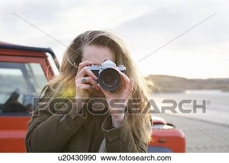 Stock Image - Mid adult woman photographing with SLR in coastal parking lot. Fotosearch