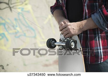 Mid section of young man holding skateboard View Large Photo Image Stock Image - Mid section of young man holding skateboard. Fotosearch