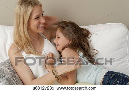 Stock Photography - Mother and daughter laughing on sofa. Fotosearch