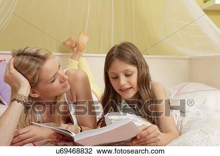 Mother and daughter lying on bed looking at notebook View Large Photo Image Stock Image - Mother and daughter lying on bed looking at notebook. Fotosearch