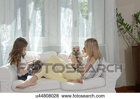 Stock Photo - Mother and daughter on sofa petting cats. Fotosearch