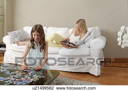 Stock Image - Mother on sofa with cat, daughter doing jigsaw. Fotosearch