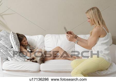 Stock Photograph - Mother photographing daughter and cat on sofa. Fotosearch
