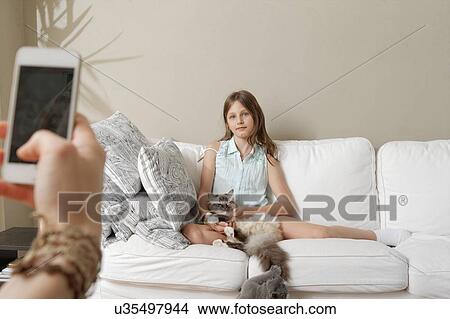 Picture - Mother photographing daughter with cat on sofa. Fotosearch