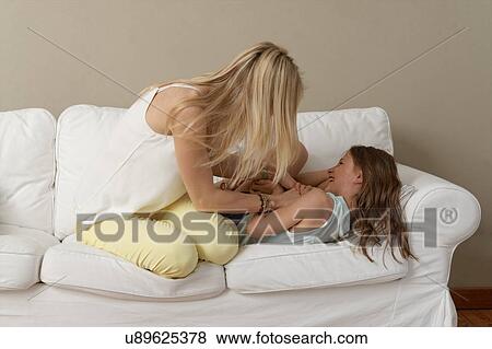Mother tickling daughter on sofa View Large Photo Image Stock Photo - Mother tickling daughter on sofa. Fotosearch