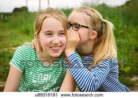 Nine year old girl whispering to sister in field View Large Photo Image Stock Image - Nine year old girl whispering to sister in field. Fotosearch