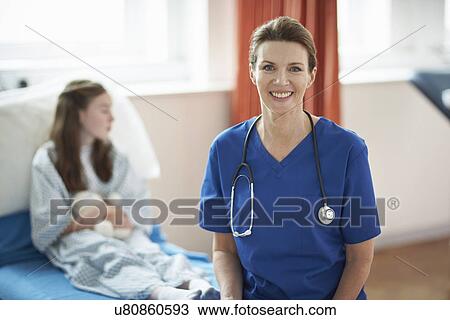 Stock Image - Nurse sitting on end of patient's bed. Fotosearch