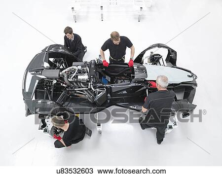 Stock Image - Overhead view of engineers assembling supercar in sports car factory. Fotosearch